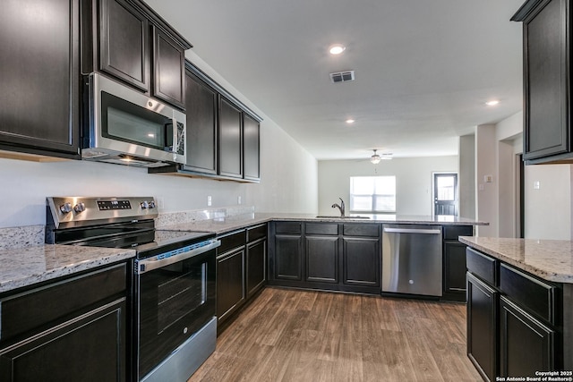 kitchen with sink, ceiling fan, appliances with stainless steel finishes, light stone counters, and dark hardwood / wood-style flooring