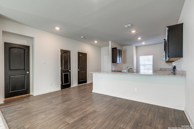 kitchen featuring sink, dark hardwood / wood-style floors, light stone countertops, and kitchen peninsula