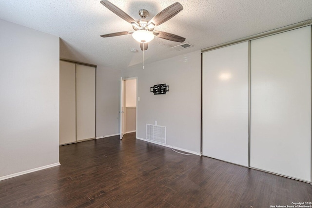 unfurnished bedroom featuring dark hardwood / wood-style flooring, multiple closets, a textured ceiling, and ceiling fan