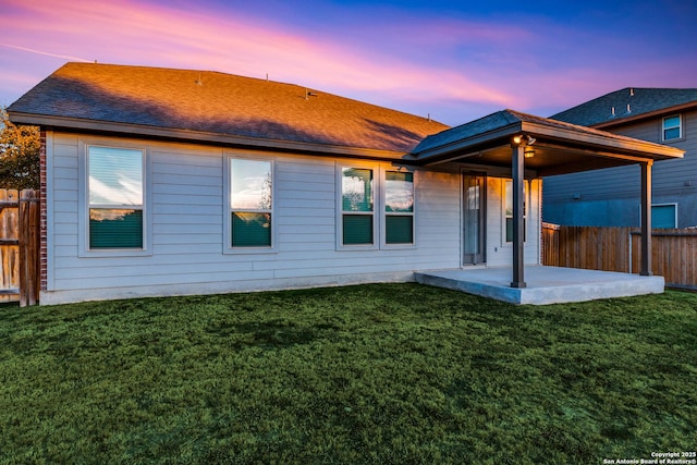 back house at dusk with a patio and a lawn