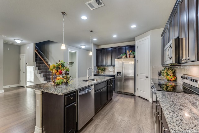 kitchen with pendant lighting, sink, a kitchen island with sink, stainless steel appliances, and light wood-type flooring