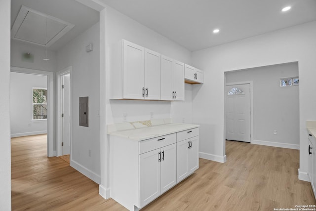 kitchen featuring electric panel, light stone countertops, white cabinets, and light wood-type flooring