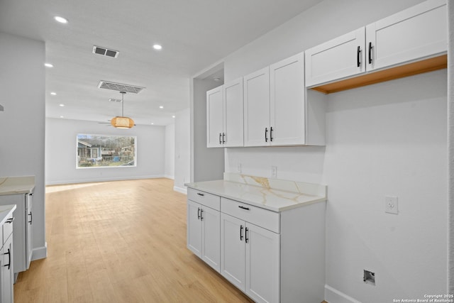 kitchen featuring pendant lighting, light stone countertops, light hardwood / wood-style flooring, and white cabinets