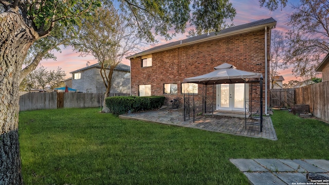 back house at dusk featuring a gazebo, a yard, a patio, and french doors