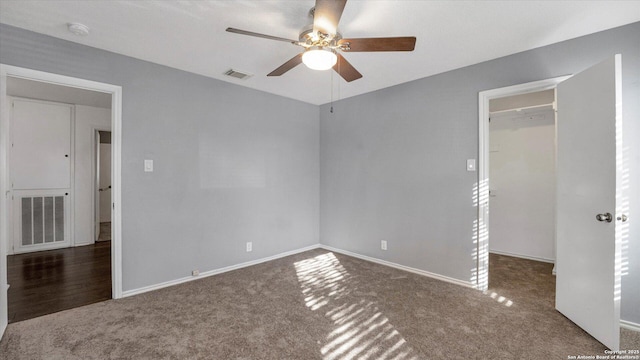 unfurnished bedroom with ceiling fan, a walk in closet, dark carpet, and a closet