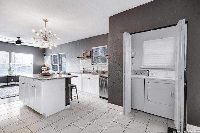 kitchen with sink, stainless steel dishwasher, a kitchen island, washing machine and dryer, and white cabinets