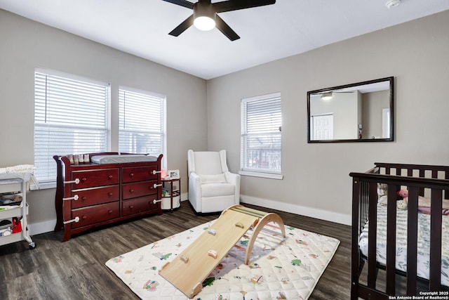 bedroom with a crib, dark wood-type flooring, and ceiling fan