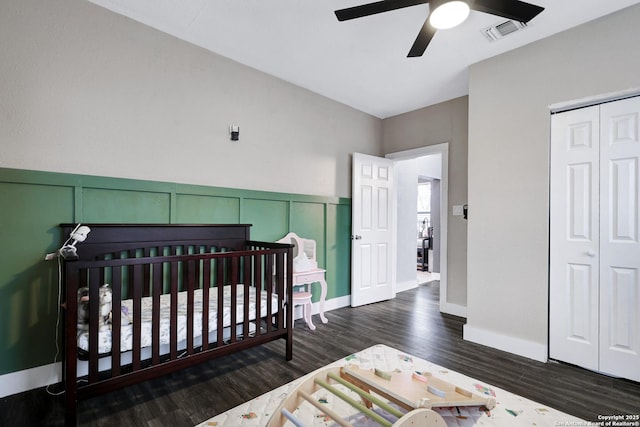 bedroom with a nursery area, ceiling fan, dark wood-type flooring, and a closet