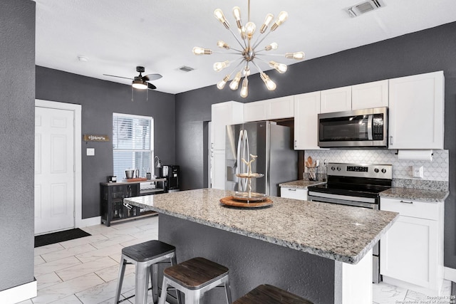 kitchen featuring light stone countertops, stainless steel appliances, a center island, and white cabinets