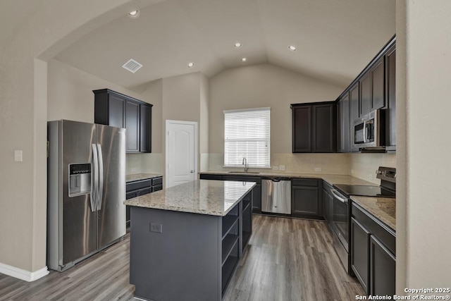 kitchen featuring a kitchen island, appliances with stainless steel finishes, wood-type flooring, sink, and light stone countertops