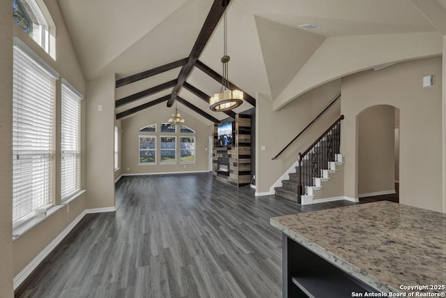 unfurnished living room with a notable chandelier, dark wood-type flooring, lofted ceiling with beams, and plenty of natural light