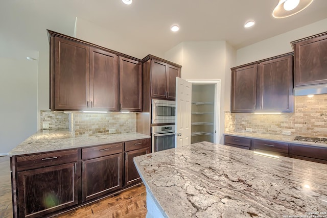 kitchen featuring dark brown cabinetry, appliances with stainless steel finishes, light stone countertops, and decorative backsplash