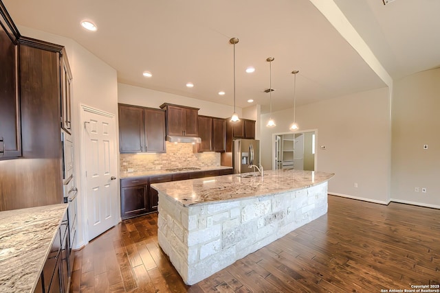 kitchen featuring appliances with stainless steel finishes, pendant lighting, decorative backsplash, light stone counters, and a spacious island