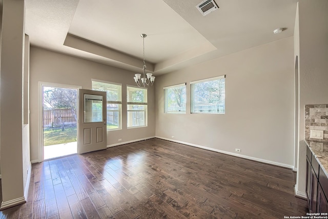 unfurnished dining area featuring a raised ceiling, dark hardwood / wood-style flooring, and an inviting chandelier