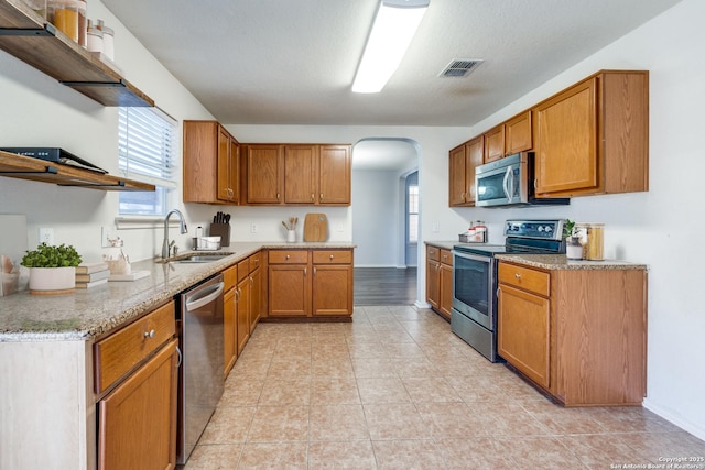 kitchen featuring sink, light tile patterned floors, light stone counters, stainless steel appliances, and a textured ceiling