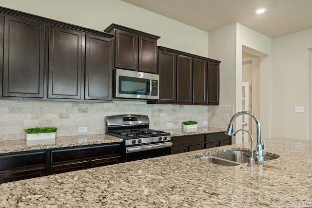 kitchen with appliances with stainless steel finishes, tasteful backsplash, sink, light stone countertops, and dark brown cabinets