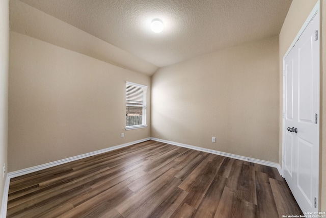 empty room with vaulted ceiling, a textured ceiling, and dark hardwood / wood-style flooring