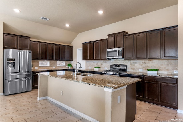 kitchen with appliances with stainless steel finishes, lofted ceiling, sink, a kitchen island with sink, and light stone counters