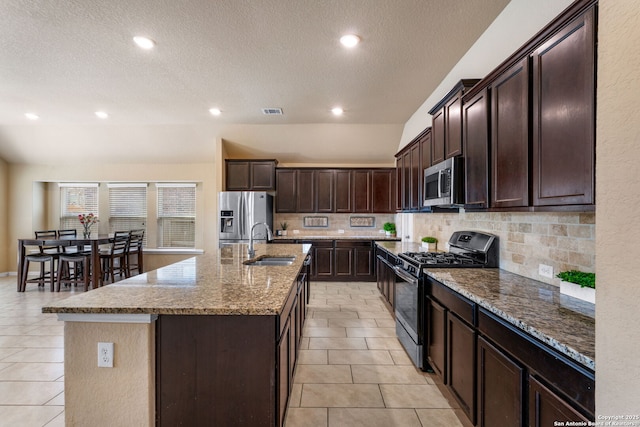 kitchen with light tile patterned floors, a center island with sink, sink, and appliances with stainless steel finishes