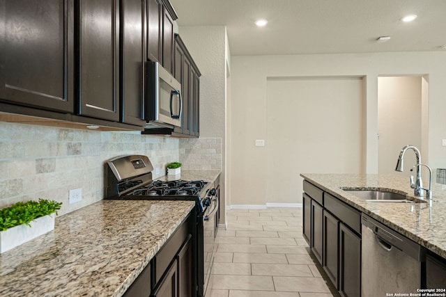 kitchen with appliances with stainless steel finishes, tasteful backsplash, sink, light stone countertops, and dark brown cabinets