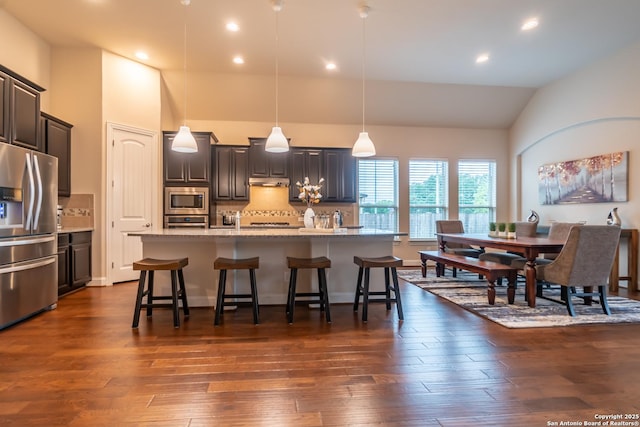 kitchen with a kitchen bar, tasteful backsplash, hanging light fixtures, an island with sink, and stainless steel appliances