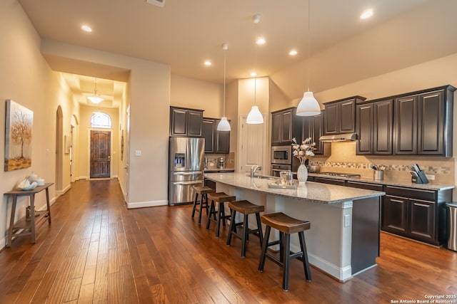 kitchen featuring a towering ceiling, appliances with stainless steel finishes, a breakfast bar, and an island with sink