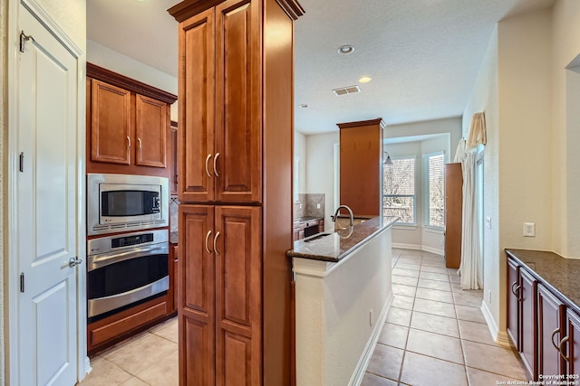 kitchen featuring appliances with stainless steel finishes, sink, light tile patterned floors, and dark stone counters