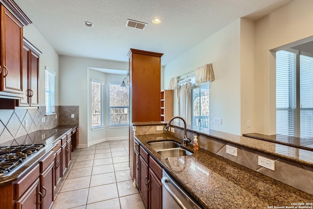 kitchen with sink, appliances with stainless steel finishes, dark stone countertops, tasteful backsplash, and a textured ceiling