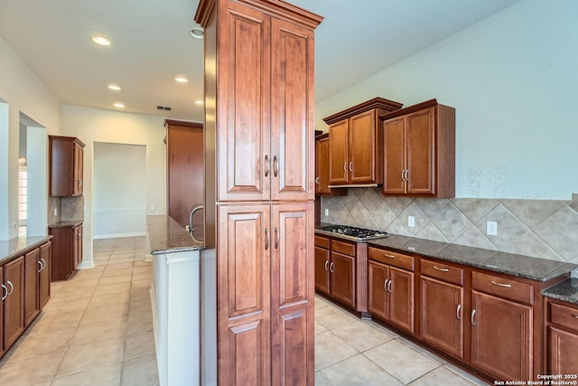 kitchen with dark stone countertops, decorative backsplash, stainless steel gas cooktop, and light tile patterned flooring