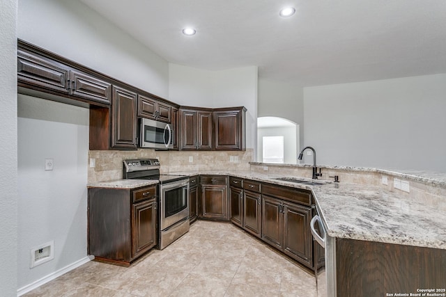 kitchen with dark brown cabinetry, sink, appliances with stainless steel finishes, kitchen peninsula, and light stone countertops