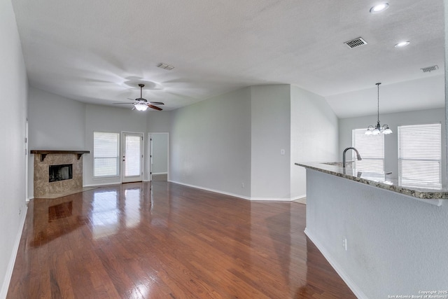 unfurnished living room featuring dark wood-type flooring, a high end fireplace, ceiling fan with notable chandelier, and plenty of natural light