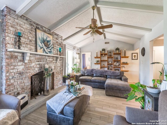 living room with ceiling fan, a fireplace, a textured ceiling, and vaulted ceiling with beams