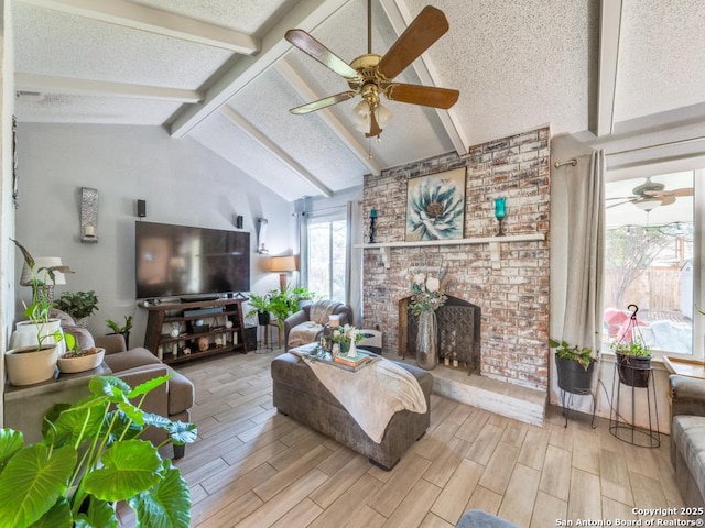 living room with vaulted ceiling with beams, a fireplace, a textured ceiling, and ceiling fan