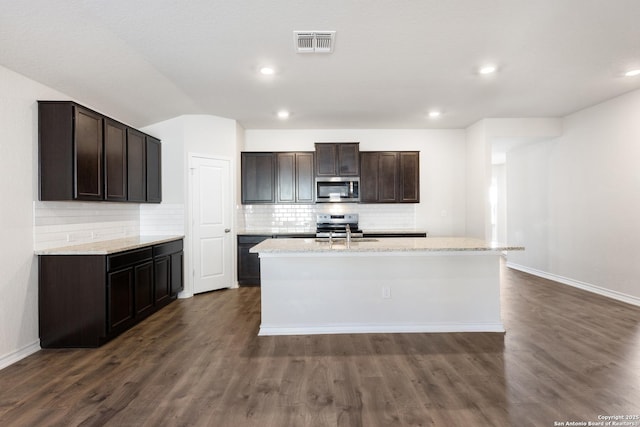 kitchen with sink, decorative backsplash, stainless steel appliances, dark brown cabinets, and a center island with sink