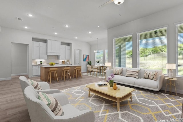 living room featuring ceiling fan with notable chandelier and light wood-type flooring