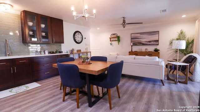 dining space with crown molding, wood-type flooring, ceiling fan with notable chandelier, and sink