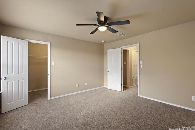 unfurnished bedroom featuring a walk in closet, light colored carpet, ceiling fan, and a closet