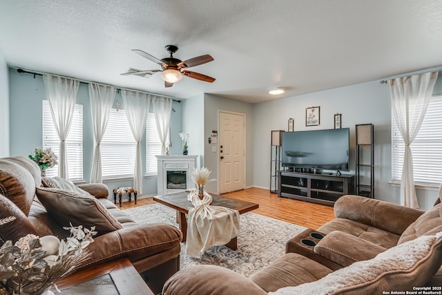 living room with ceiling fan, a textured ceiling, and light wood-type flooring