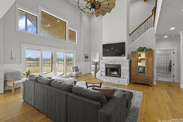 living room featuring a high ceiling, ceiling fan, a fireplace, and light hardwood / wood-style flooring