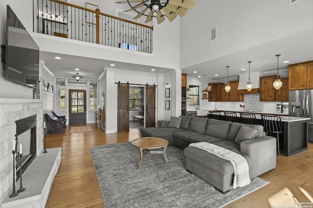 living room featuring ornamental molding, a towering ceiling, ceiling fan, a barn door, and light hardwood / wood-style floors