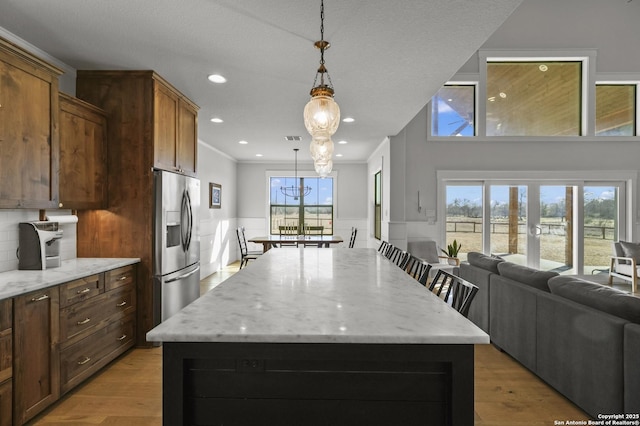 kitchen with a kitchen island, pendant lighting, light stone counters, stainless steel refrigerator with ice dispenser, and a healthy amount of sunlight