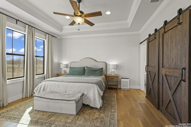 bedroom with ceiling fan, a tray ceiling, a barn door, and multiple windows