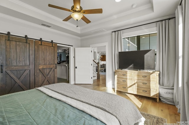 bedroom with hardwood / wood-style flooring, a spacious closet, ceiling fan, a tray ceiling, and a closet