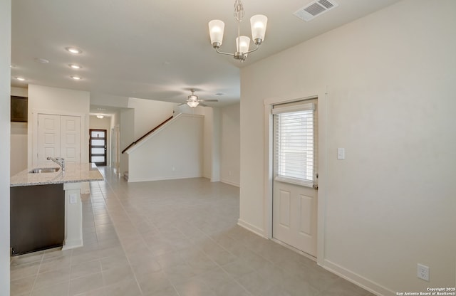 unfurnished living room featuring ceiling fan with notable chandelier, light tile patterned flooring, and sink