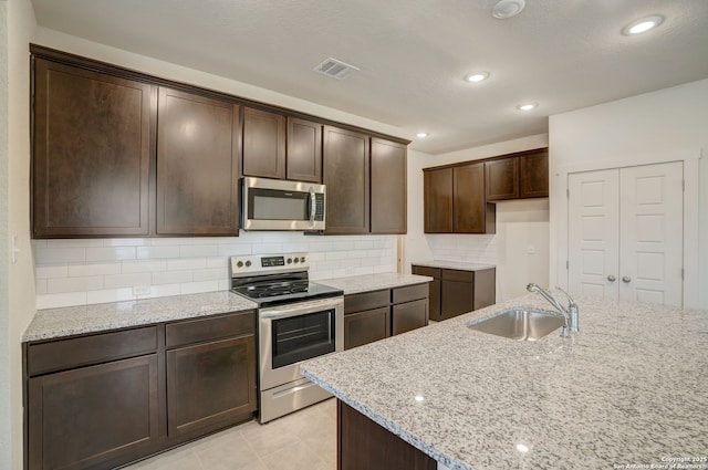 kitchen featuring sink, stainless steel appliances, light stone counters, dark brown cabinetry, and decorative backsplash