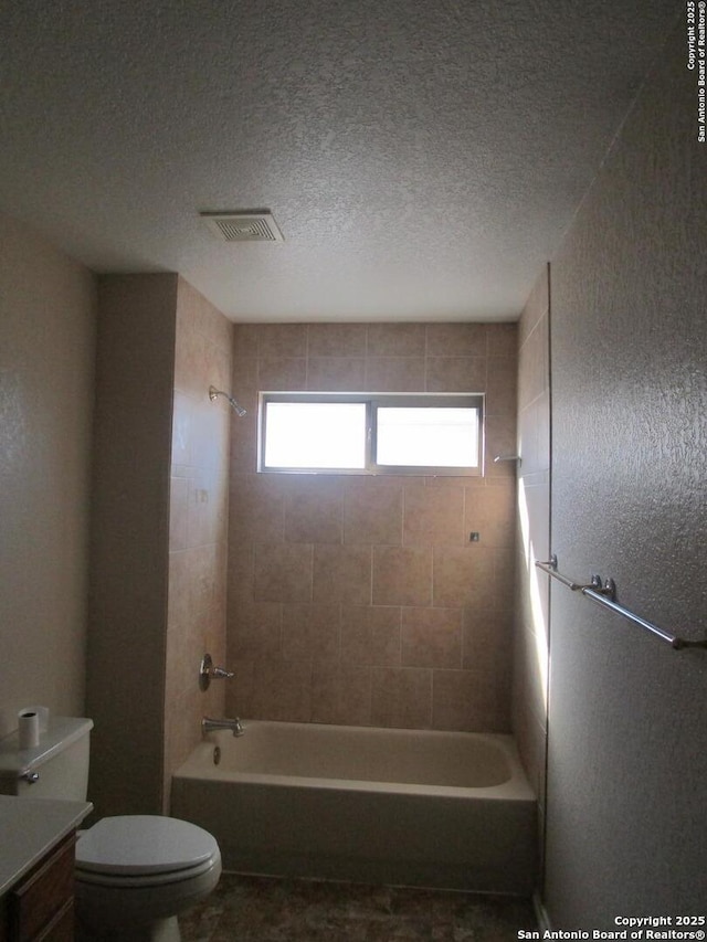 bathroom featuring tiled shower / bath, toilet, and a textured ceiling