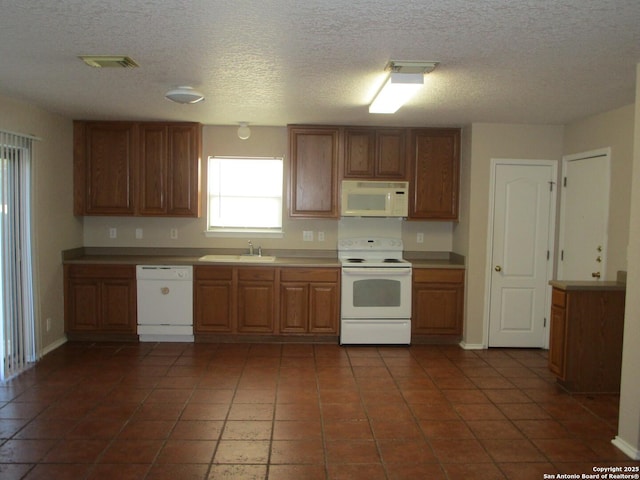 kitchen with white appliances, dark tile patterned flooring, sink, and a textured ceiling