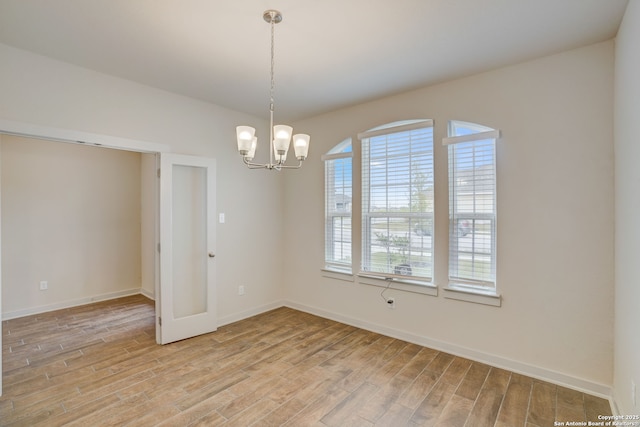 spare room with a chandelier and light wood-type flooring