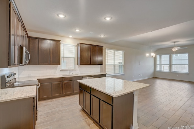 kitchen with sink, stainless steel appliances, tasteful backsplash, light stone counters, and decorative light fixtures