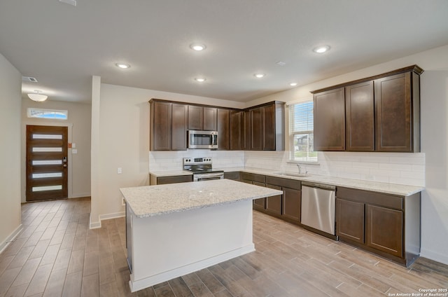 kitchen with stainless steel appliances, light stone countertops, sink, and light wood-type flooring